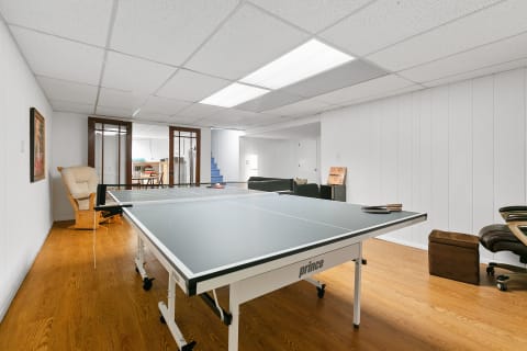 A spacious basement game room features a ping pong table, rocking chair, and modern seating.