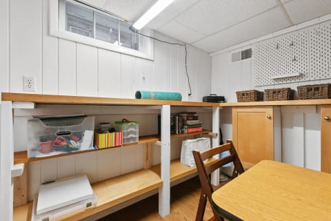 Interior view of a well-arranged basement workspace with a wooden workbench, storage containers, and a narrow window.