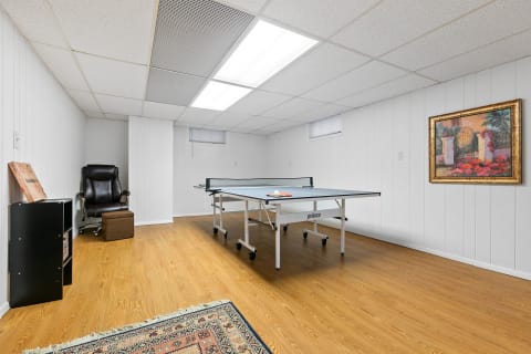 A basement room with a ping pong table, a recliner chair, and a decorative painting on the wall.