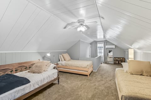 Spacious attic bedroom featuring three beds with a high slanted ceiling.