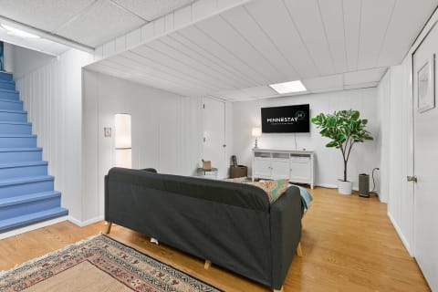 A cozy basement living room featuring a gray couch, a TV, and blue stairs.