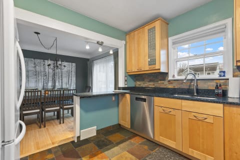 Modern kitchen with wooden cabinets and a dining area featuring tree-themed wallpaper.