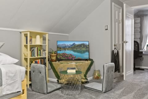 A cozy attic room featuring a TV, bookshelf, and gray floor chairs.