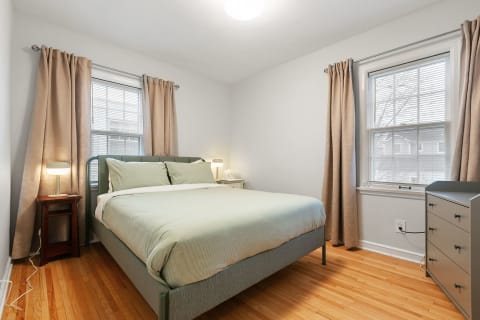 A cozy bedroom featuring a green bedspread, wooden nightstand, and modern decor.