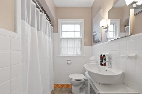 Modern bathroom with white tiles, shower curtain, oval sink, and natural light from a window.