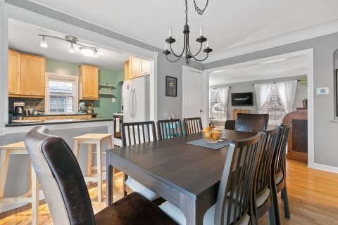Dining area with a dark wooden table, surrounding chairs, and a view of the kitchen with light wood cabinets.
