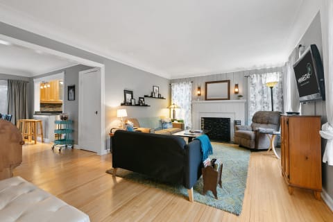 A living room featuring a dark sofa, coffee table, and fireplace, with a kitchen area visible in the background.