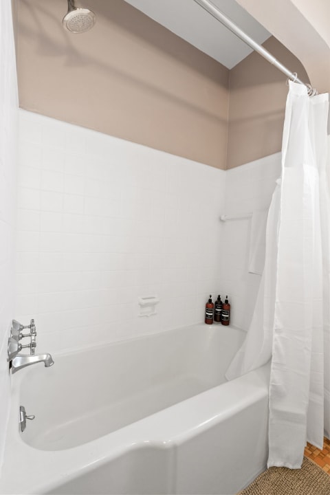 A minimalist bathroom with a white bathtub, shower curtain, and stylish bath products.