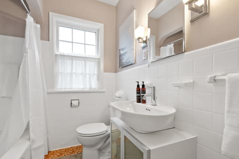 Interior view of a modern bathroom with a white shower, sink, and natural light.