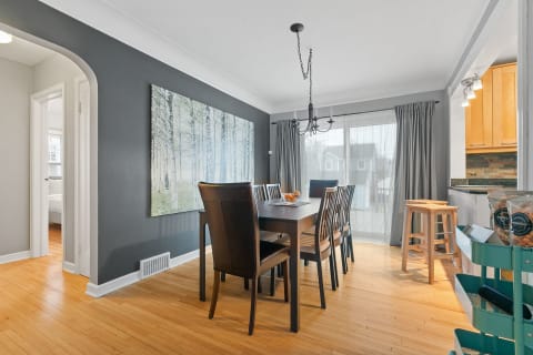 A beautifully designed dining area featuring a dark gray wall, wooden flooring, and a large forest wall art.