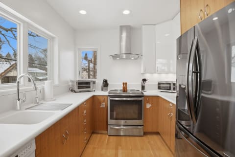A modern kitchen with wood cabinetry, stainless steel appliances, and large windows allowing natural light.