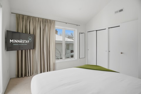 Modern bedroom with a queen bed, wall-mounted TV, and large window.