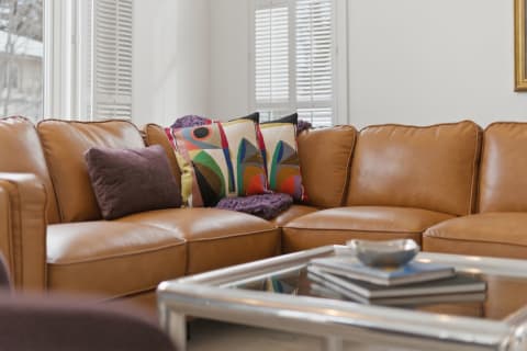 Leather sectional couch with decorative colorful pillows and a glass coffee table in a bright living room.