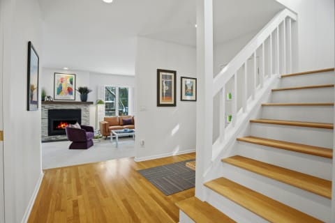 A cozy living area featuring a fireplace, staircase, and colorful decor, creating a warm atmosphere.
