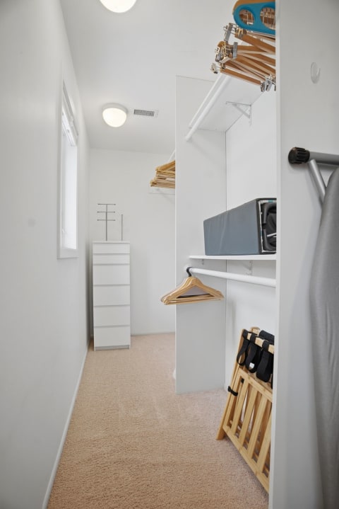 Modern walk-in closet with white walls, wooden hangers, and a shelving unit.