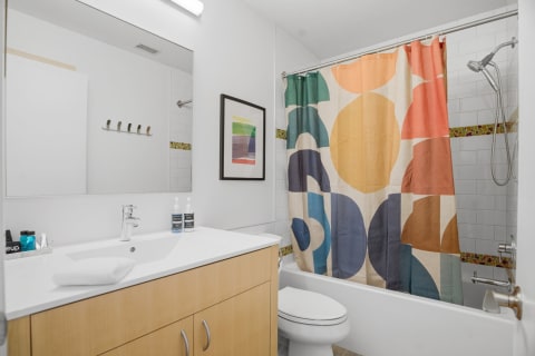 A modern bathroom with a colorful geometric shower curtain and sleek wood vanity.