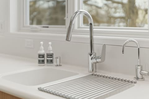Modern kitchen sink featuring chrome faucets and white countertop with soap bottles.