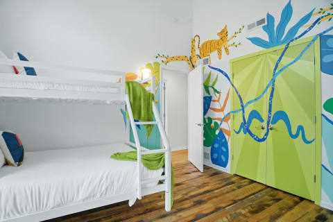 Bunk beds in a playful children's room with a bright jungle mural and vibrant green doors.