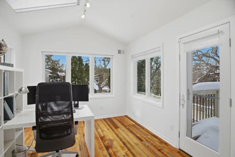 A bright home office featuring a white interior, large windows with snowy views, and a wooden floor.