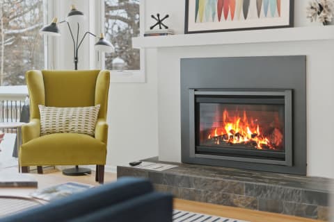 A mustard wingback chair beside a modern fireplace in a bright living room with snow outside.