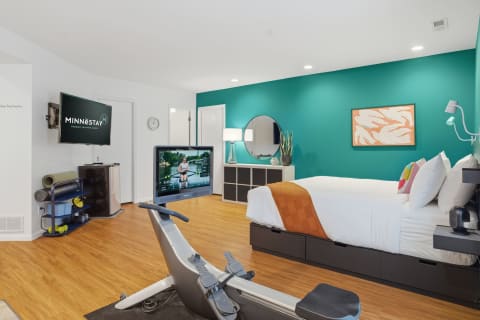 A bright bedroom with a rowing machine, teal accent wall, and modern furnishings.