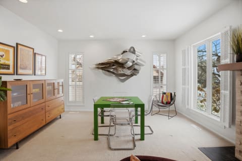 A bright modern room with a green table, transparent chairs, artistic wall sculpture, and large windows.