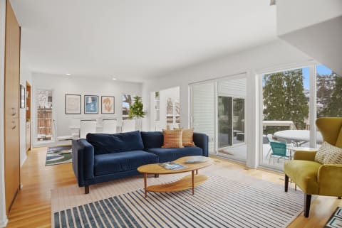 Living room with a navy sofa, coffee table, and dining area visible through glass doors.