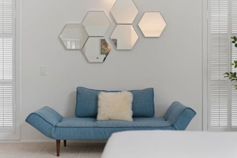 Modern blue daybed with a white pillow and hexagonal mirrors on the wall.