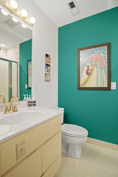 A stylish bathroom featuring a turquoise wall, marble vanity, and framed artwork.