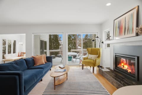 A modern living room with a navy sofa, yellow armchair, fireplace, and sliding glass doors leading to a snowy balcony.
