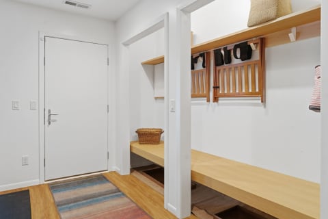A simple entryway with a white door, wooden bench, and organized storage for accessories.