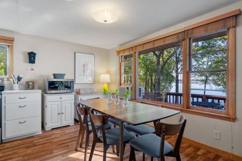 Cozy dining area featuring a table, chairs, and large windows overlooking trees and water.