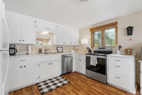 A bright kitchen featuring white cabinets, marble countertops, and wood flooring, with modern appliances and warm natural light.