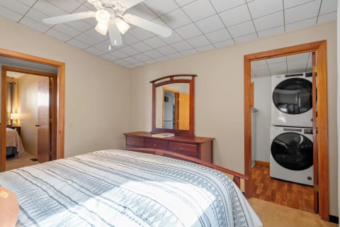 A well-lit bedroom with a bed, dresser, and doorway to a laundry area.