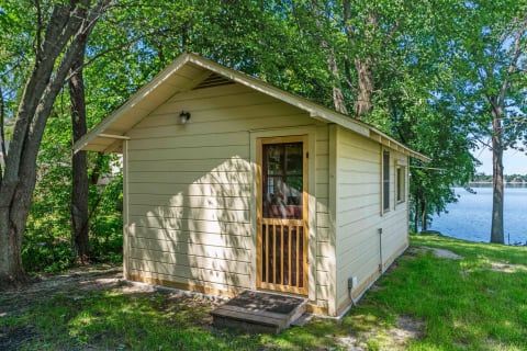 Small yellow cabin beside a calm lake surrounded by trees.