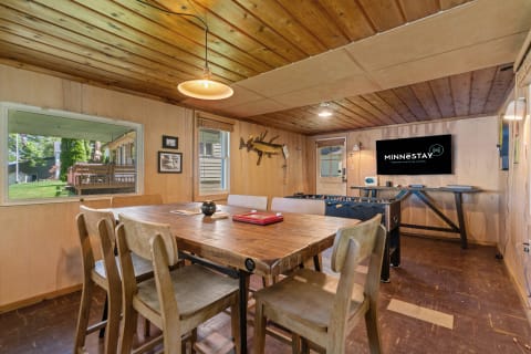 A cozy interior featuring a dining table, foosball table, and large television in a wooden room.