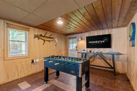 A game room with a foosball table, wooden paneling, TV with MINNESTAY logo, and dartboard.