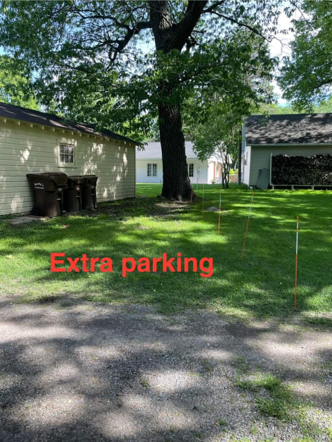 Designated extra parking area with orange stakes, trash bins, and trees.