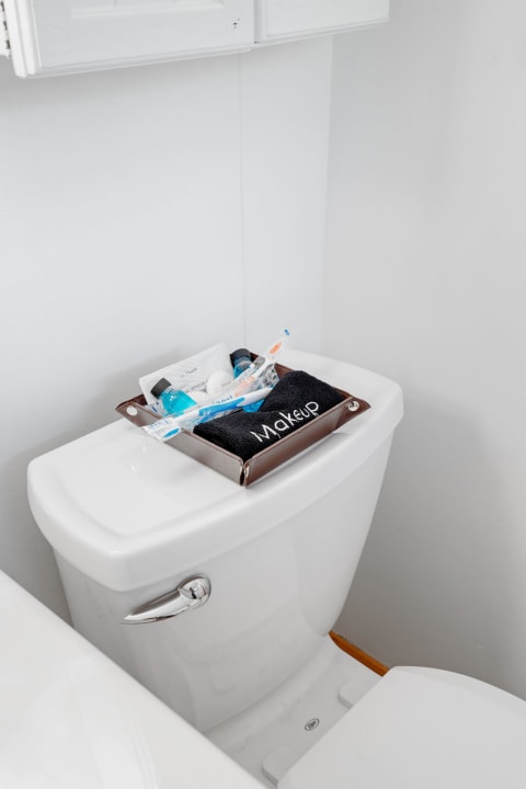 A brown tray with makeup items on top of a white toilet in a minimal bathroom.