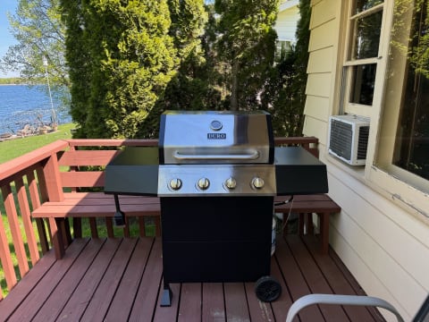 A black and stainless steel grill on a wooden deck beside a lake.