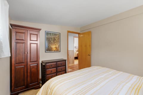 Cozy bedroom with wooden wardrobe and dresser, featuring a striped duvet and a forest photograph on the wall.