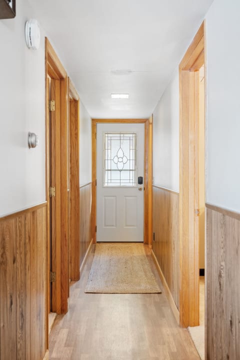 A narrow hallway with wooden wainscoting and a decorative glass door at the end.