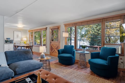 Living room with teal chairs, hardwood floors, and large windows overlooking a lake.