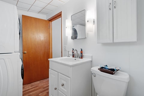 Compact bathroom with a white vanity, washer and dryer, and wooden door.