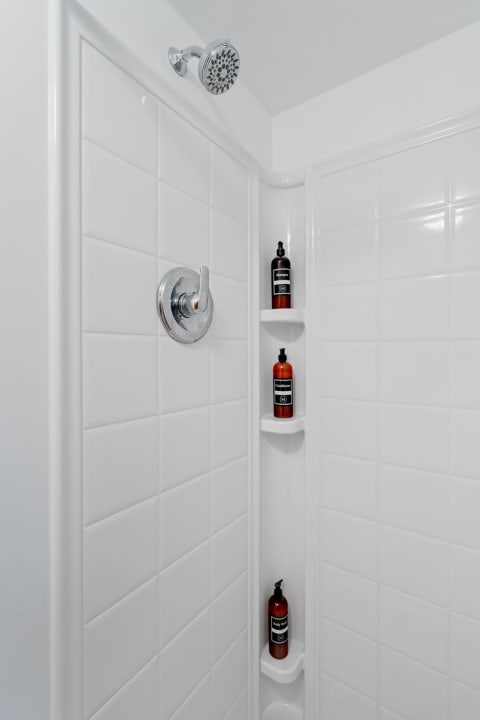 Interior of a shower with tiled walls and personal care products on a shelf.