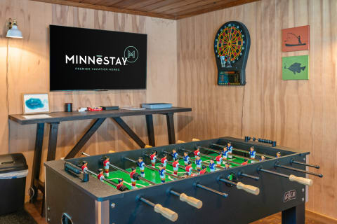 A foosball table in a recreational space with a TV displaying a vacation home logo and a dartboard on the wall.