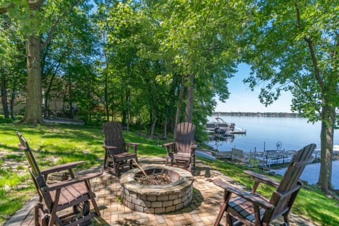 Outdoor fire pit area with adirondack chairs near a lake.