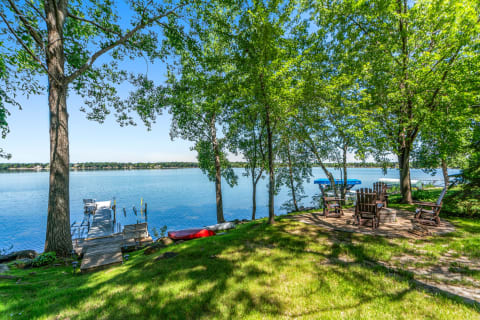A lakeside view featuring a dock and Adirondack chairs surrounded by trees.