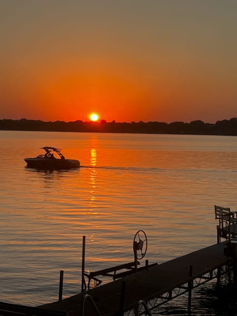 A sunset view over a lake with a boat and a dock in the foreground.