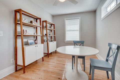 A minimalist dining area with a round white table and blue chairs, accompanied by modern wooden shelves.